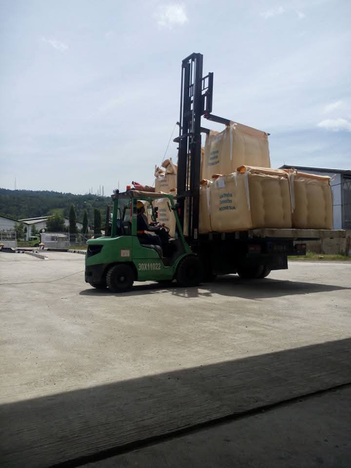 Forklift hijau sedang menangani muatan besar di area industri